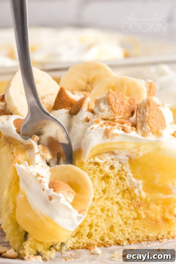 This delicious banana pudding poke cake recipe is quick and easy and perfect for a potluck. Use a cake mix for this beautiful poke cake dessert! A fork taking a piece of banana pudding poke cake, showing the layers of cake, pudding, whipped cream, and bananas