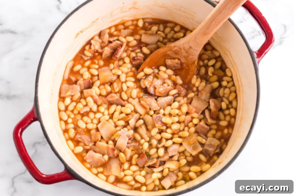 These homemade baked beans are baked in a delicious tangy sweet and savory sauce of brown sugar, maple syrup, ketchup, and apple cider vinegar. stirring the bean mixture with a wooden spoon