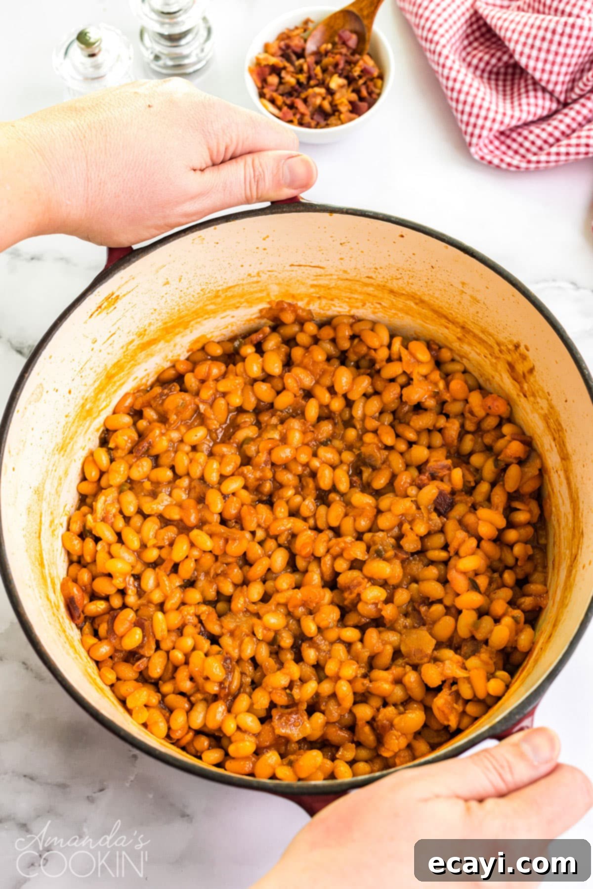 These homemade baked beans are baked in a delicious tangy sweet and savory sauce of brown sugar, maple syrup, ketchup, and apple cider vinegar. dutch oven full of homemade baked beans being carried to the table