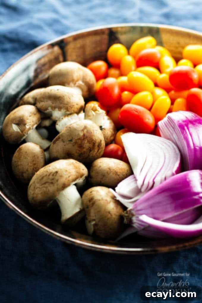 Tender Grilled Chicken Kebabs 3 A close up photo of fresh ingredients for kabobs, including mushrooms, chopped red onion, and grape tomatoes in a bowl.