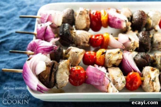Tender Grilled Chicken Kebabs 5 A beautifully arranged close up of raw marinated chicken skewers, artfully threaded with red onion, grape tomatoes, and mushrooms, ready for the grill.