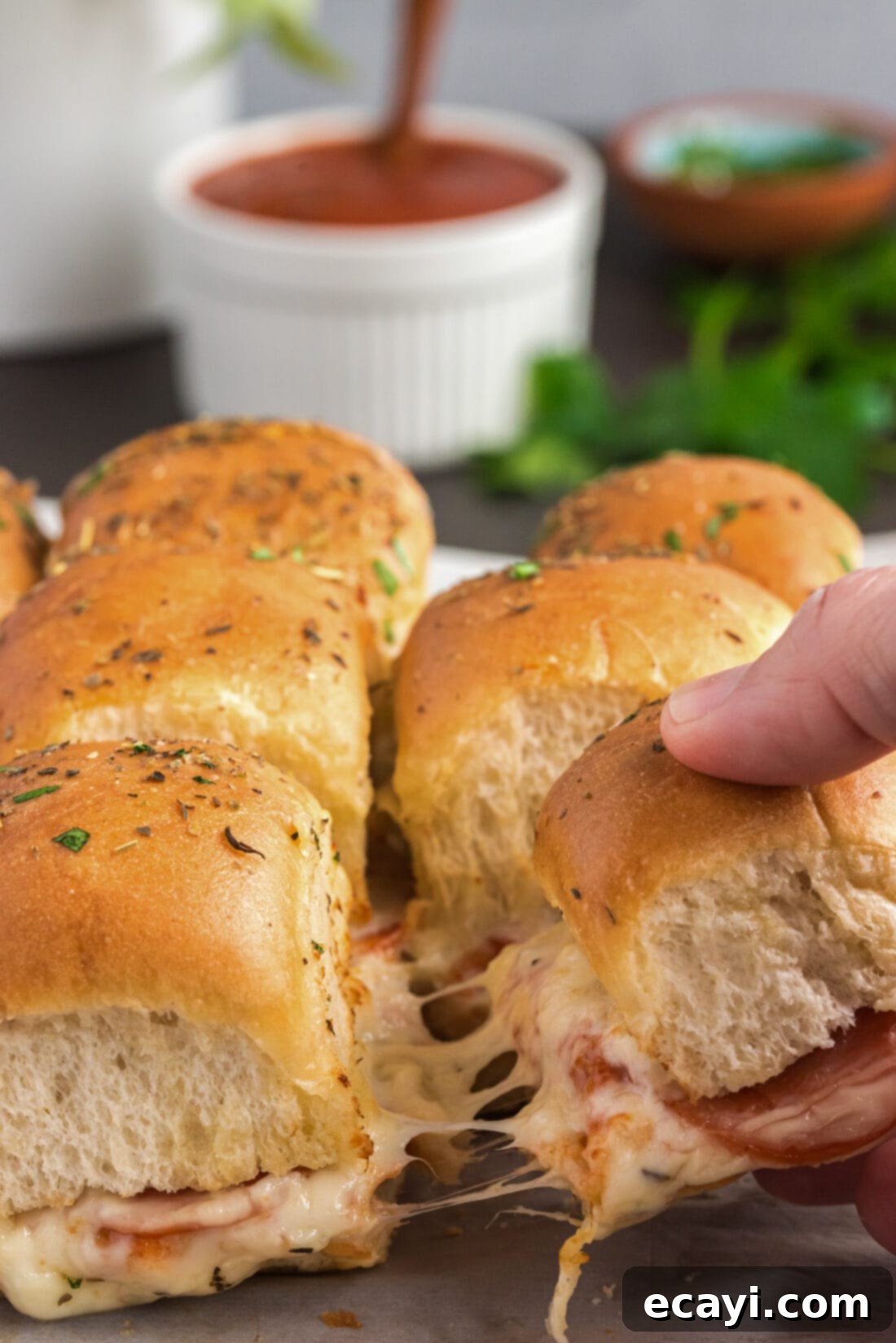 Cheesy Pizza Bites 3 A hand pulling a single pizza slider from a tray of baked sliders