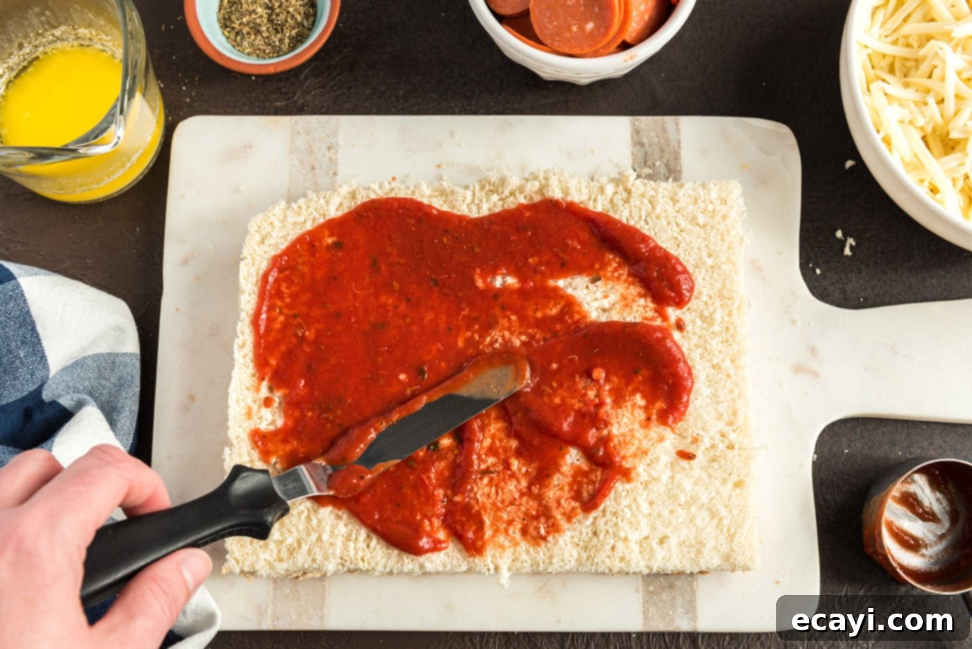 Cheesy Pizza Bites 6 Pizza sauce being spread evenly over the bottom halves of slider buns in a baking dish
