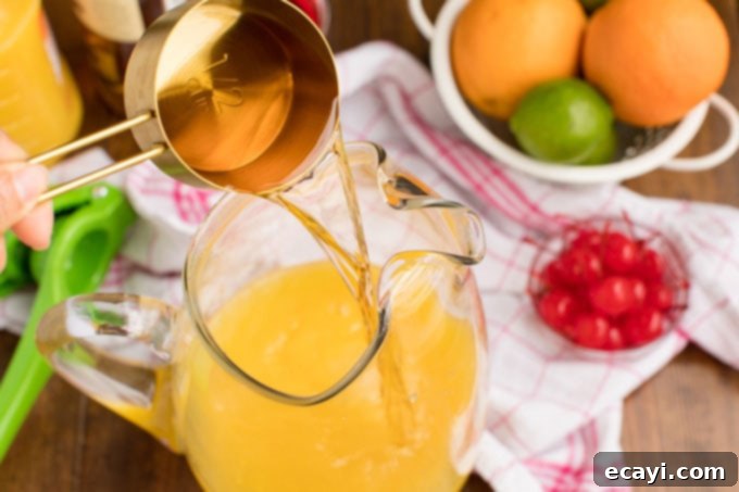Punch of Paradise 6 Pouring gold rum into a pitcher containing a vibrant mix of orange and pineapple juice