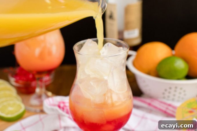 Punch of Paradise 9 Slowly pouring rum punch mixture into a glass with grenadine and ice to create a sunset effect