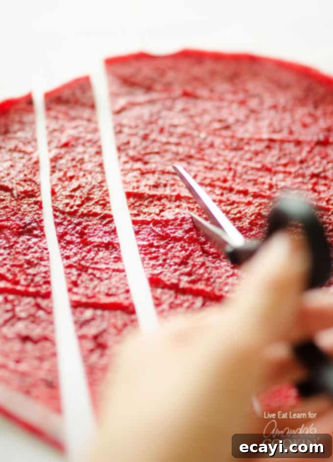 Simple DIY Fruit Leather 3 A close up of homemade fruit roll ups being cut into strips on parchment paper.