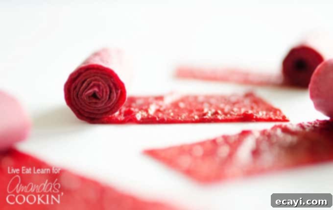 Simple DIY Fruit Leather 5 A close up of homemade fruit roll ups being rolled up with parchment paper, showing the finished product.