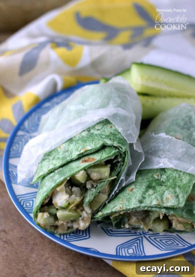 Sun-Drenched Mediterranean Wrap 2 Two halves of a Mediterranean veggie wrap in wax paper resting next to each other on a blue and white plate.