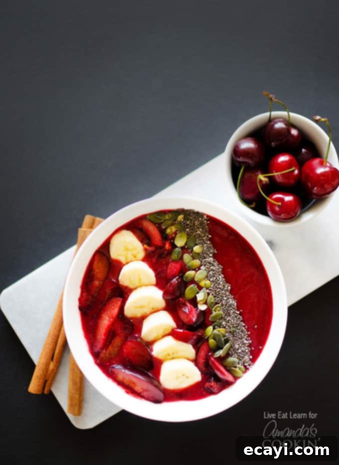 Sun-Kissed Stone Fruit Bowl 2 An overhead photo of a beautifully arranged stone fruit smoothie in a white bowl, topped with artistic slices of plums, fresh cherries, banana, and a sprinkle of mixed nuts and seeds, ready to be enjoyed.