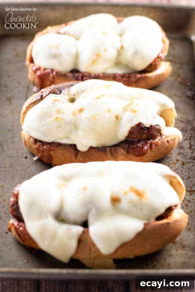 Sweet and Smoky Slow Cooker Meatball Sub Heroes 3 A close-up photo of three freshly assembled slow cooker BBQ meatball subs, each topped with golden-melted provolone cheese.