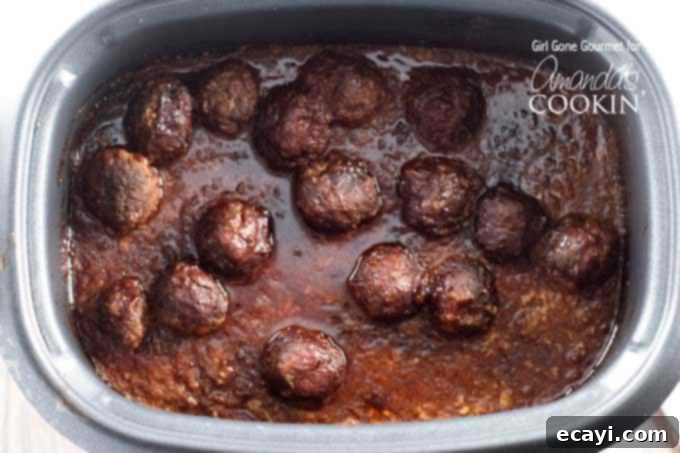 Sweet and Smoky Slow Cooker Meatball Sub Heroes 4 An overhead photo of perfectly shaped meatballs simmering in a rich barbecue sauce in a slow cooker.