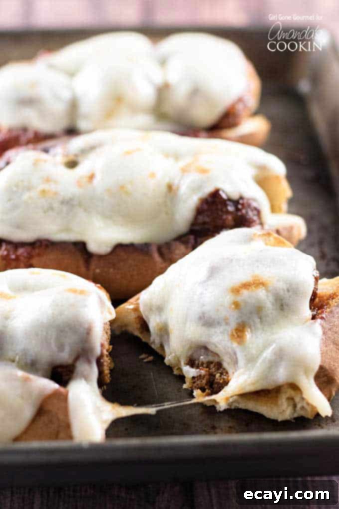 Sweet and Smoky Slow Cooker Meatball Sub Heroes 5 A close-up photo of a slow cooker BBQ meatball sub, cut in half, showcasing the succulent meatballs and melted provolone cheese, with two other subs in the background.