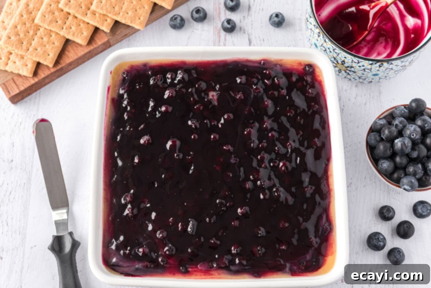 Creamy No-Bake Blueberry Cheesecake 10 blueberry pie filling on top of cheesecake in a pan, ready for final chill.