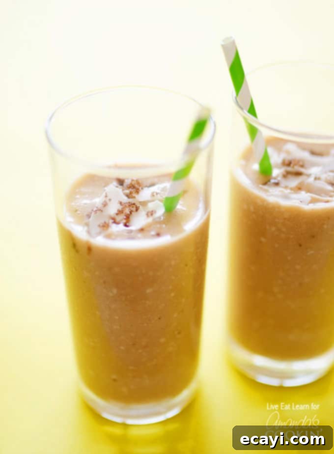 Creamy Coconut Bliss 2 A close up of two tall clear glasses filled with cozy coconut smoothie and served with a green and white striped straw.