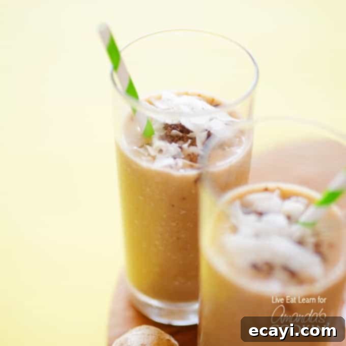Creamy Coconut Bliss 3 Two tall clear glasses filled with a cozy coconut smoothie and served with a green and white striped straw.