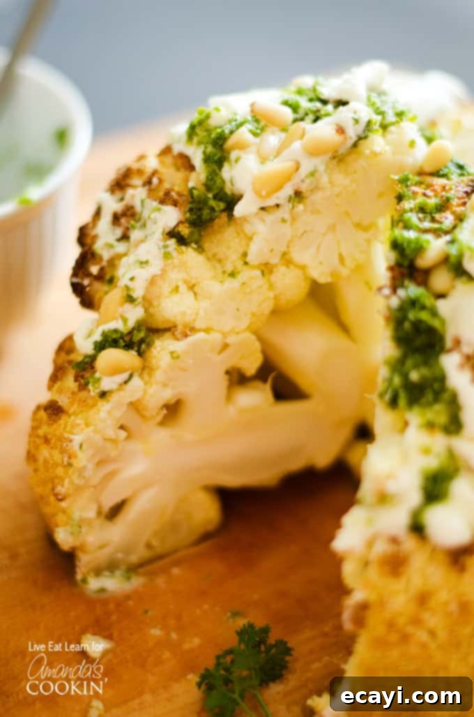 The Ultimate Whole Roasted Cauliflower 2 A close up of the center of a whole roasted cauliflower topped with whipped feta and herb sauce on a wooden cutting board.
