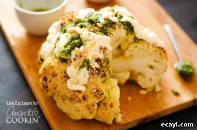 The Ultimate Whole Roasted Cauliflower 5 A close up of a whole roasted cauliflower topped with whipped feta and herb sauce on a wooden cutting board.