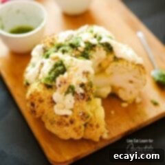 The Ultimate Whole Roasted Cauliflower 6 A close up of a whole roasted cauliflower topped with whipped feta and herb sauce on a wooden cutting board.