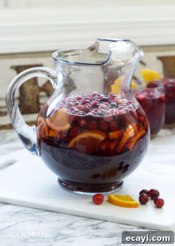 Serve this cranberry sangria to your guests and they will be asking for the recipe and for seconds! #amandascookin #cocktails #sangria #cranberry #orangejuice #christmasrecipes #christmascocktails #thanksgivingcocktails #thanksgivingdrinks Two glasses of sparkling cranberry sangria with orange slices and fresh cranberries, ready to be served at a festive gathering.