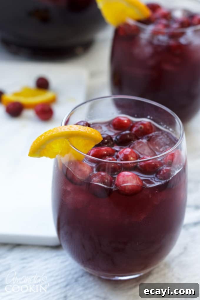 Looking for a great holiday adult beverage? Serve this cranberry sangria to your guests and they will be asking for the recipe and for seconds! #amandascookin #cocktails #sangria #cranberry #orangejuice #christmasrecipes #christmascocktails #thanksgivingcocktails #thanksgivingdrinks A glass of cranberry sangria garnished with a fresh orange slice and cranberries, showcasing its beautiful color and inviting presentation.