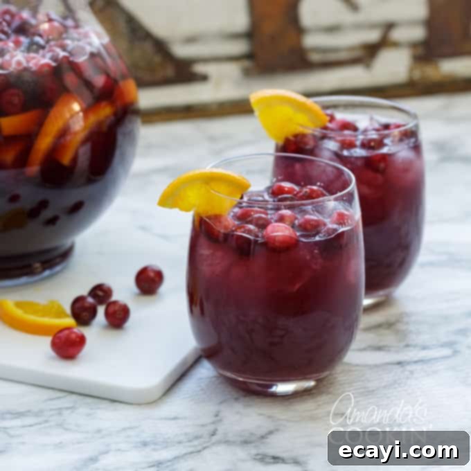 Looking for a great holiday adult beverage? Serve this cranberry sangria to your guests and they will be asking for the recipe and for seconds! #amandascookin #cocktails #sangria #cranberry #orangejuice #christmasrecipes #christmascocktails #thanksgivingcocktails #thanksgivingdrinks Two glasses of cranberry sangria on a rustic wooden surface, garnished with fresh orange wedges, ready for a cozy toast.