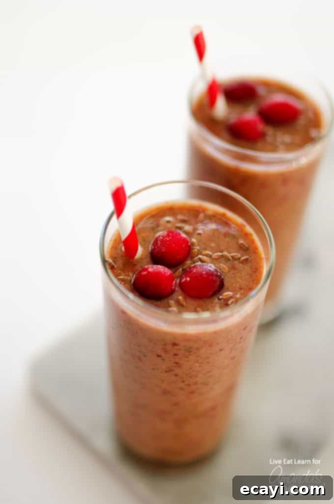 Holiday Reset: Cranberry Cleanse Smoothie 2 A close up overhead of two cranberry smoothies with cranberries on top and served with a straw.