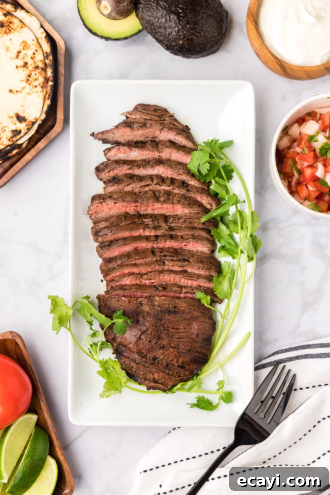 Treat yourself to Mexican at home with this authentic carne asada! Tender and delicious Mexican grilled steak is perfect for tacos, burrito bowls and more! Cooked marinated Carne Asada on a platter with salsa, sour cream and tortillas on the side