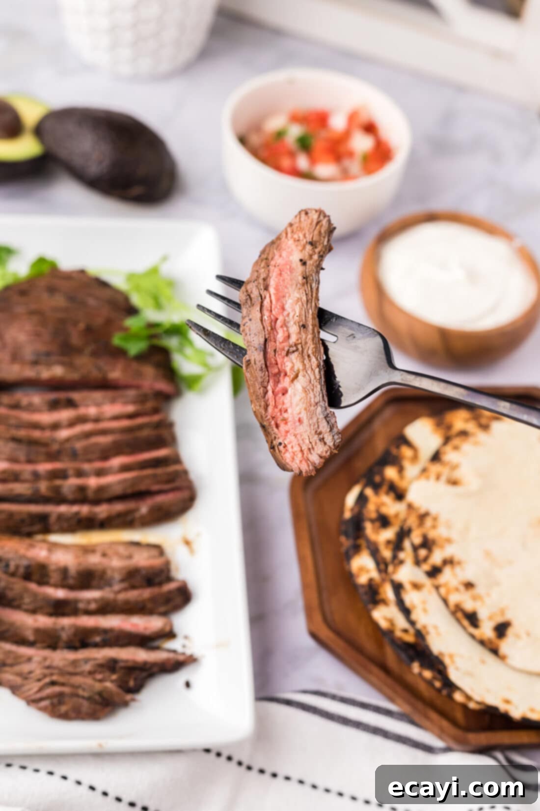 Treat yourself to Mexican at home with this authentic carne asada! Tender and delicious Mexican grilled steak is perfect for tacos, burrito bowls and more! Piece of Carne Asada on a fork with carne asada in the background and other toppings