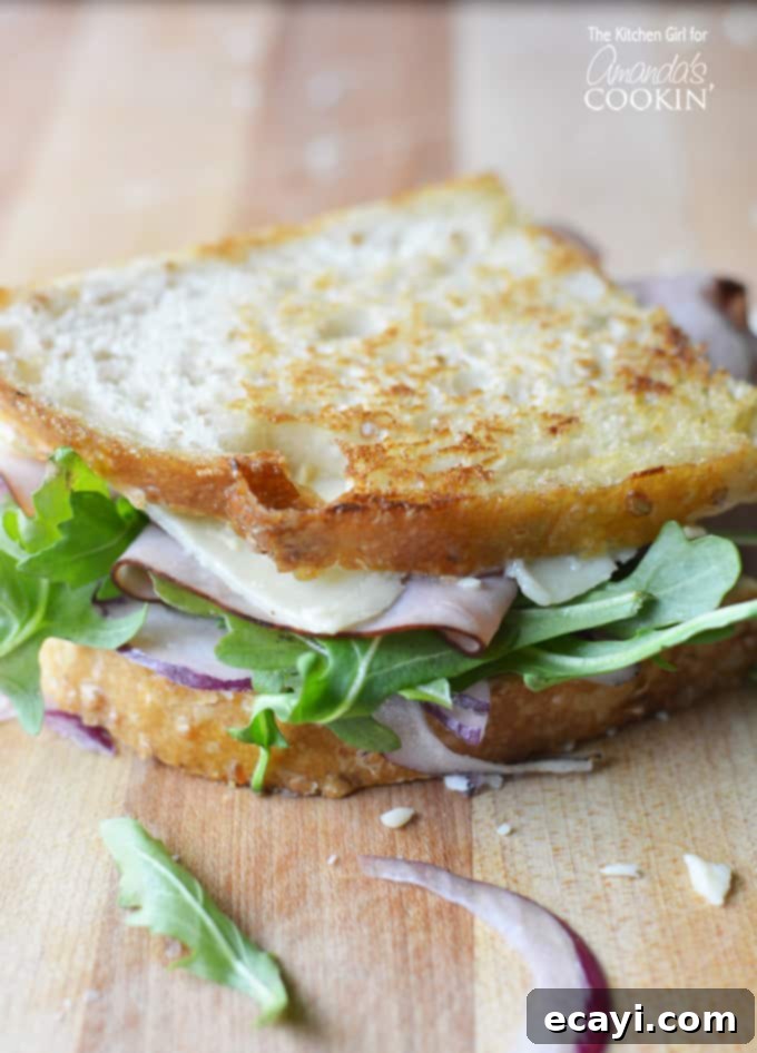 Warm Cheddar, Ham & Arugula Melt 2 A close up of a perfectly golden-brown toasted cheddar, ham, and arugula sandwich, sliced diagonally to reveal the luscious melted cheese, savory ham, and fresh green arugula within.