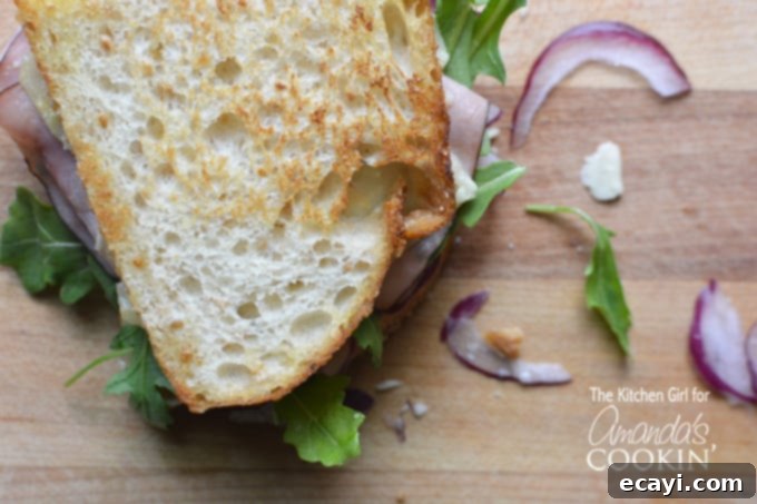 Warm Cheddar, Ham & Arugula Melt 4 An overhead close up view of a Toasted Cheddar, Ham, and Arugula Sandwich, showcasing the golden-brown crust and fresh ingredients.