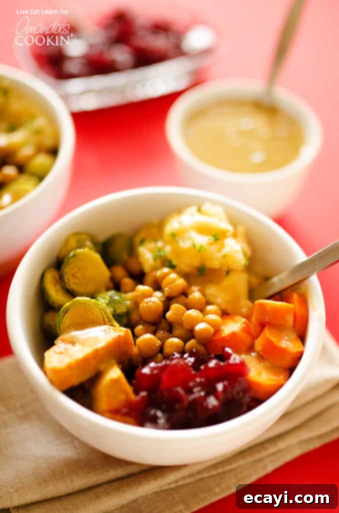 Ultimate Thanksgiving Leftovers Bowl 2 A vibrant Thanksgiving leftovers bowl brimming with roasted chickpeas, sweet potatoes, Brussels sprouts, carrots, alongside creamy mashed potatoes, tart cranberry sauce, and rich gravy.