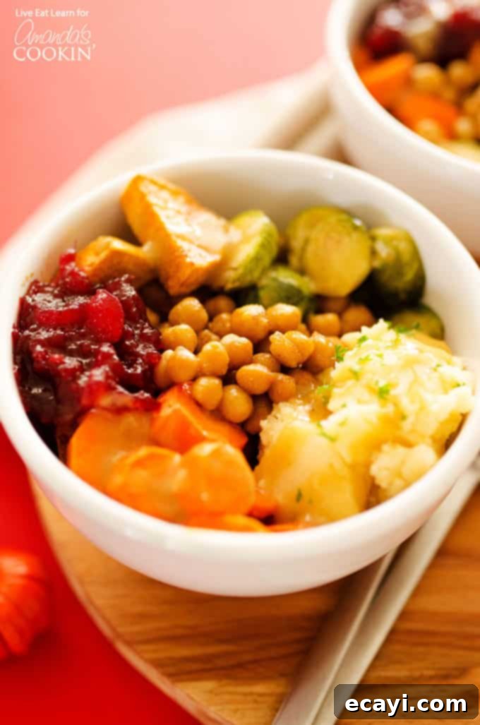 Ultimate Thanksgiving Leftovers Bowl 3 A top-down view of a Thanksgiving leftovers bowl featuring roasted chickpeas, sweet potatoes, Brussels sprouts, and carrots, artfully arranged around a dollop of mashed potatoes and cranberry sauce, with gravy drizzled over everything.