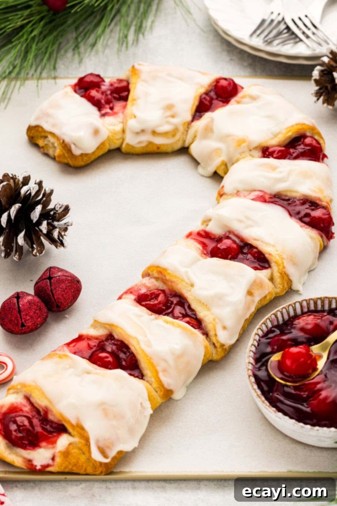 Peppermint Swirl Danish 11 Full view of a beautifully baked Candy Cane Danish, glistening with white glaze and vibrant red cherry filling, presented on a white plate ready for the holidays