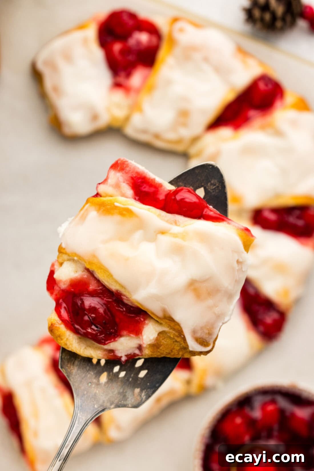 Peppermint Swirl Danish 3 A perfectly sliced portion of Candy Cane Danish being held above the main pastry, revealing the luscious layers of cream cheese and cherry filling