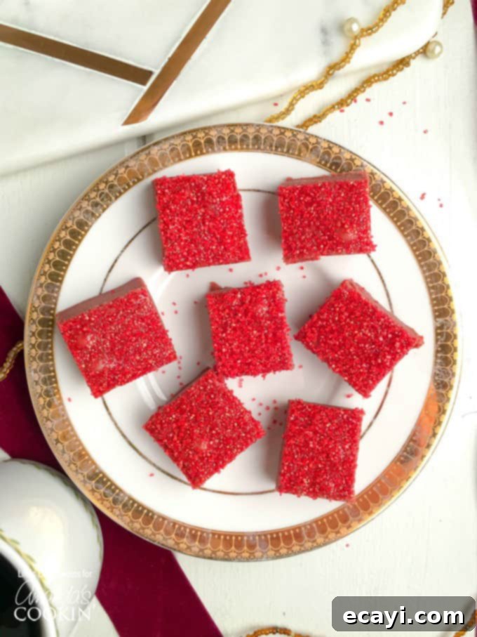 Decadent Red Velvet Fudge 3 Close-up of freshly made red velvet fudge squares, sprinkled with decorative red sugar, resting on an elegant white and gold plate.