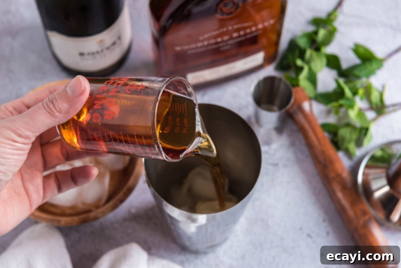 Minty Sparkle 6 pouring bourbon into cocktail shaker with mint and ice
