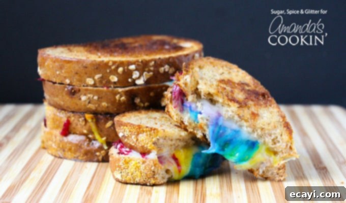 Who says you shouldn't play with your food? Make some fun food this St. Patrick's Day with this rainbow grilled cheese! Perfect for unicorn lovers too! #unicorn #rainbow #cutefood #cheese #stpatricksday #spring #sandwich Colorful Rainbow Grilled Cheese sandwich on a plate, cut open to show distinct layers of vibrant cheese.