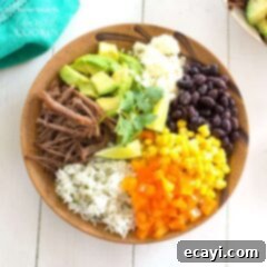 Naked Burrito 6 An overhead of a brown bowl filled with white rice, bell pepper, corn, black beans, crumbled queso fresco, avocado, lime and cooked beef.