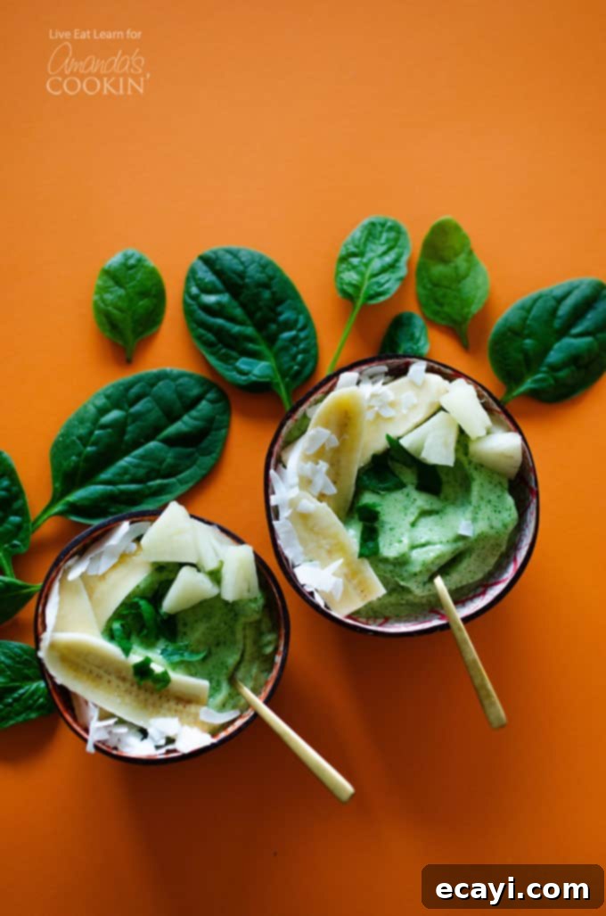 Vibrant Pineapple Power Bowl 2 An overhead of two pineapple spinach smoothie bowls with spinach leaves on the table.