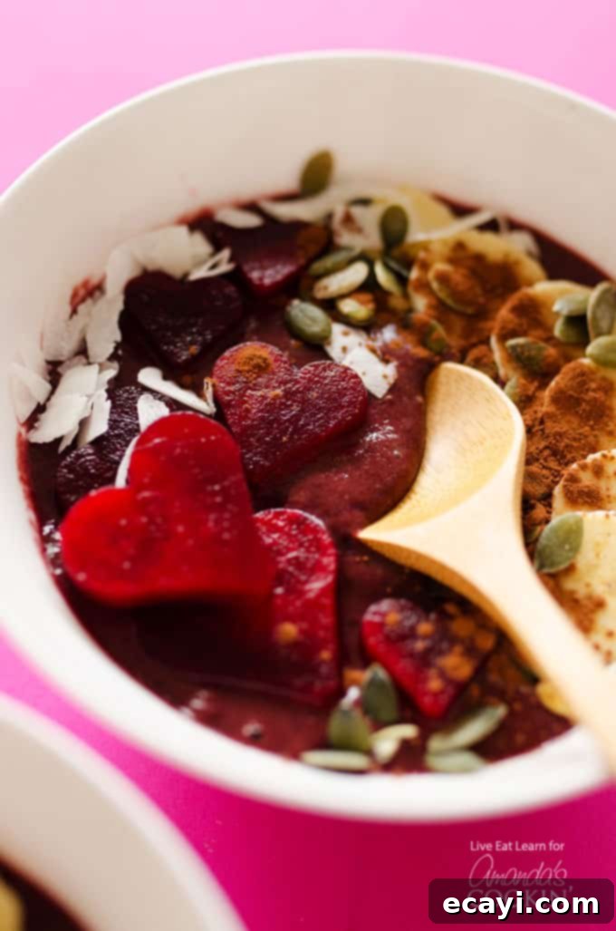 Decadent Red Velvet Smoothie Bowls 2 A close up of a white bowl filled with a red velvet smoothie and a wooden spoon.