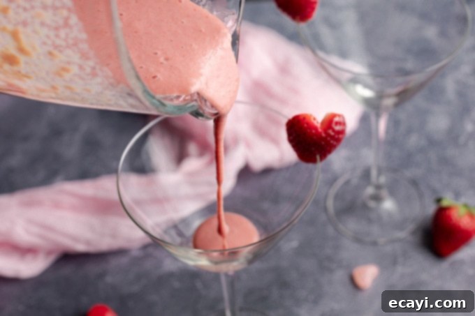 This Pink Mudslide uses fresh strawberries and vanilla ice cream along with Irish cream, coffee liqueur, and vodka for an amazing dessert Valentine's drink! Pouring the strawberry mixture into the martini glass, forming the first layer of the Pink Mudslide