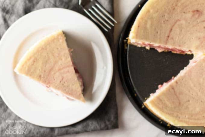 Luscious Strawberry Swirl Cheesecake 5 A mouth-watering slice of strawberry swirled cheesecake resting on a white plate, positioned next to the entire baked cheesecake, showcasing its elegant appearance.