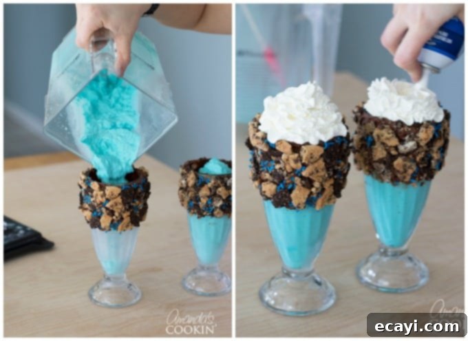 Cookie Monster Freakshakes are fun blue milkshakes topped with Cookie Monster cookies and surrounded by chocolate chip cookie pieces! #cookiemonster #cookiemonstershake #cookiemonsterparty #cookiemonsterrecipes #cookiemonsterfood #freakshake #cookies #icecream #milkshake #shakerecipes #sesamestreet #blueshakes  A vibrant blue Cookie Monster freak shake mixture being poured into a decorated glass, topped with whipped cream. This image illustrates the final assembly step before adding cookies and sprinkles.