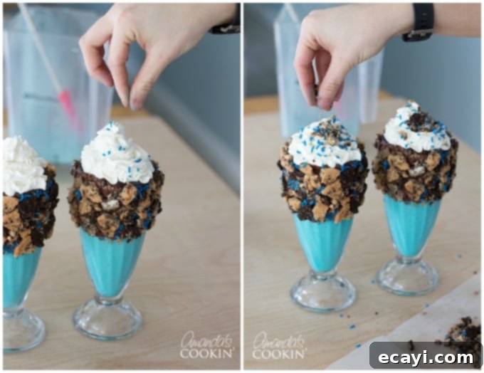 Cookie Monster Freakshakes are fun blue milkshakes topped with Cookie Monster cookies and surrounded by chocolate chip cookie pieces! #cookiemonster #cookiemonstershake #cookiemonsterparty #cookiemonsterrecipes #cookiemonsterfood #freakshake #cookies #icecream #milkshake #shakerecipes #sesamestreet #blueshakes  A close-up of a Cookie Monster Freak Shake, showing the whipped cream top adorned with blue sprinkles and leftover cookie crumbles. This detail emphasizes the rich texture and colorful toppings of the dessert.
