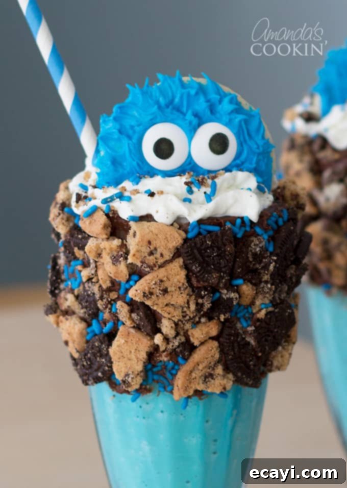 Cookie Monster Freakshakes are fun blue milkshakes topped with Cookie Monster cookies and surrounded by chocolate chip cookie pieces! #cookiemonster #cookiemonstershake #cookiemonsterparty #cookiemonsterrecipes #cookiemonsterfood #freakshake #cookies #icecream #milkshake #shakerecipes #sesamestreet #blueshakes  A perfectly assembled Cookie Monster Freak Shake, showing off its tall structure, blue milkshake, whipped cream, cookie crumbles, and the iconic Cookie Monster sugar cookie, all ready to be enjoyed. The presentation is vibrant and enticing.