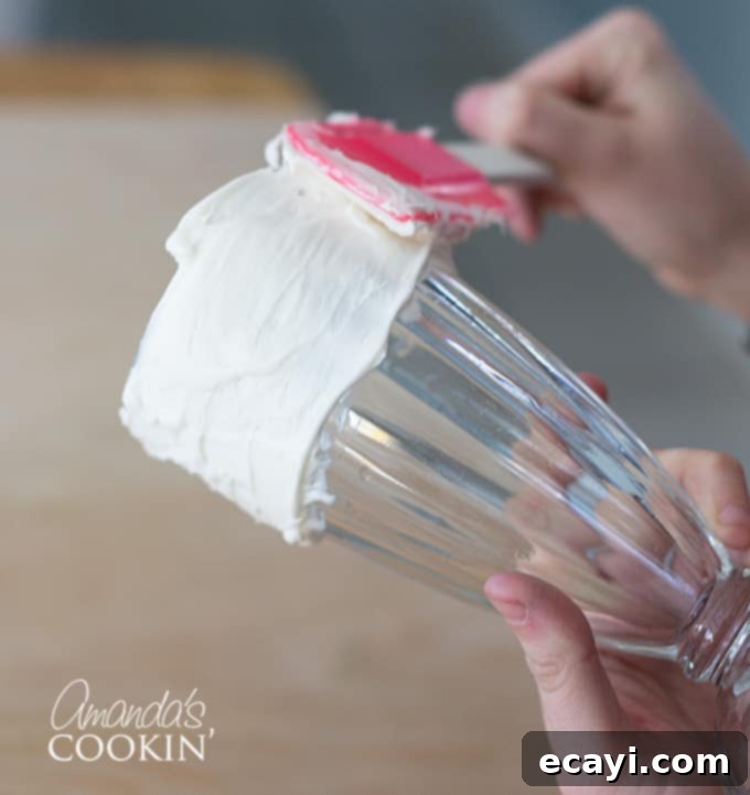 How to make Elmo Freakshakes, step 2 Applying a thick layer of vanilla frosting to the rim of a milkshake glass, preparing it for sprinkles.