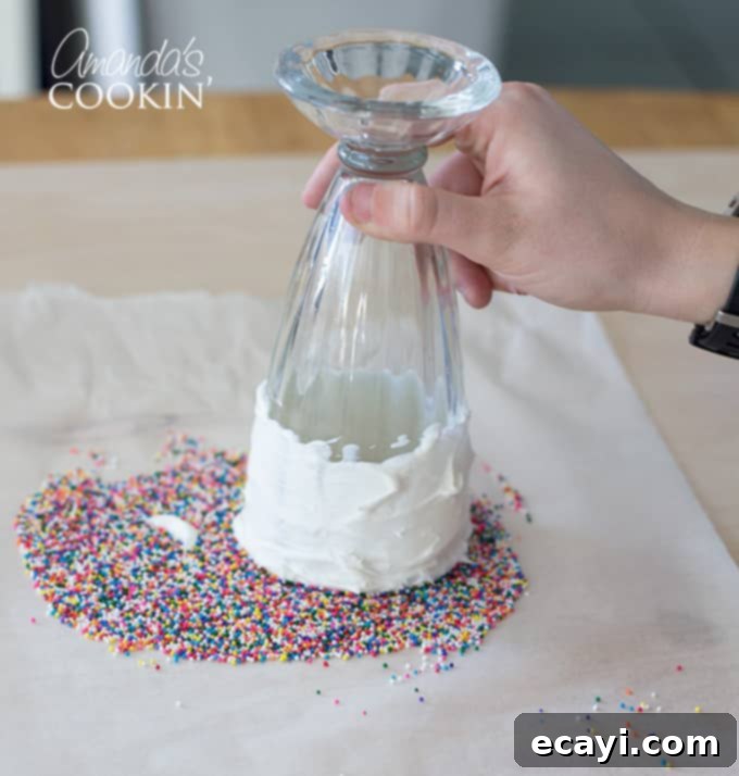 Dipping milkshake glass into sprinkles- Elmo Freakshakes step A milkshake glass being carefully dipped into a bed of colorful sprinkles on a plate, creating a festive frosted rim.