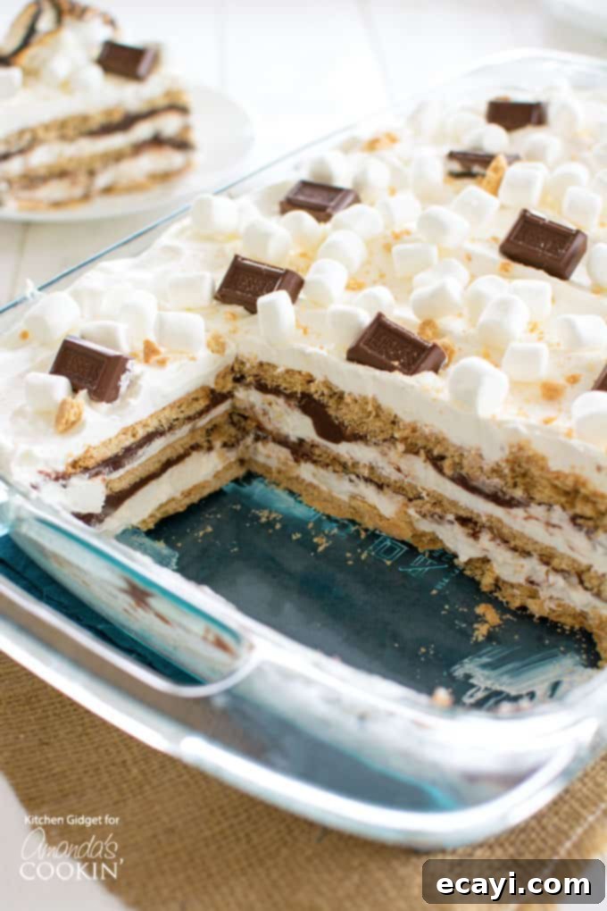 Inside the S'mores Icebox Cake: Layers of graham crackers, marshmallow cream, and chocolate ganache. sliced s'mores icebox cake layered in a glass pan, showing graham crackers, cream, and ganache