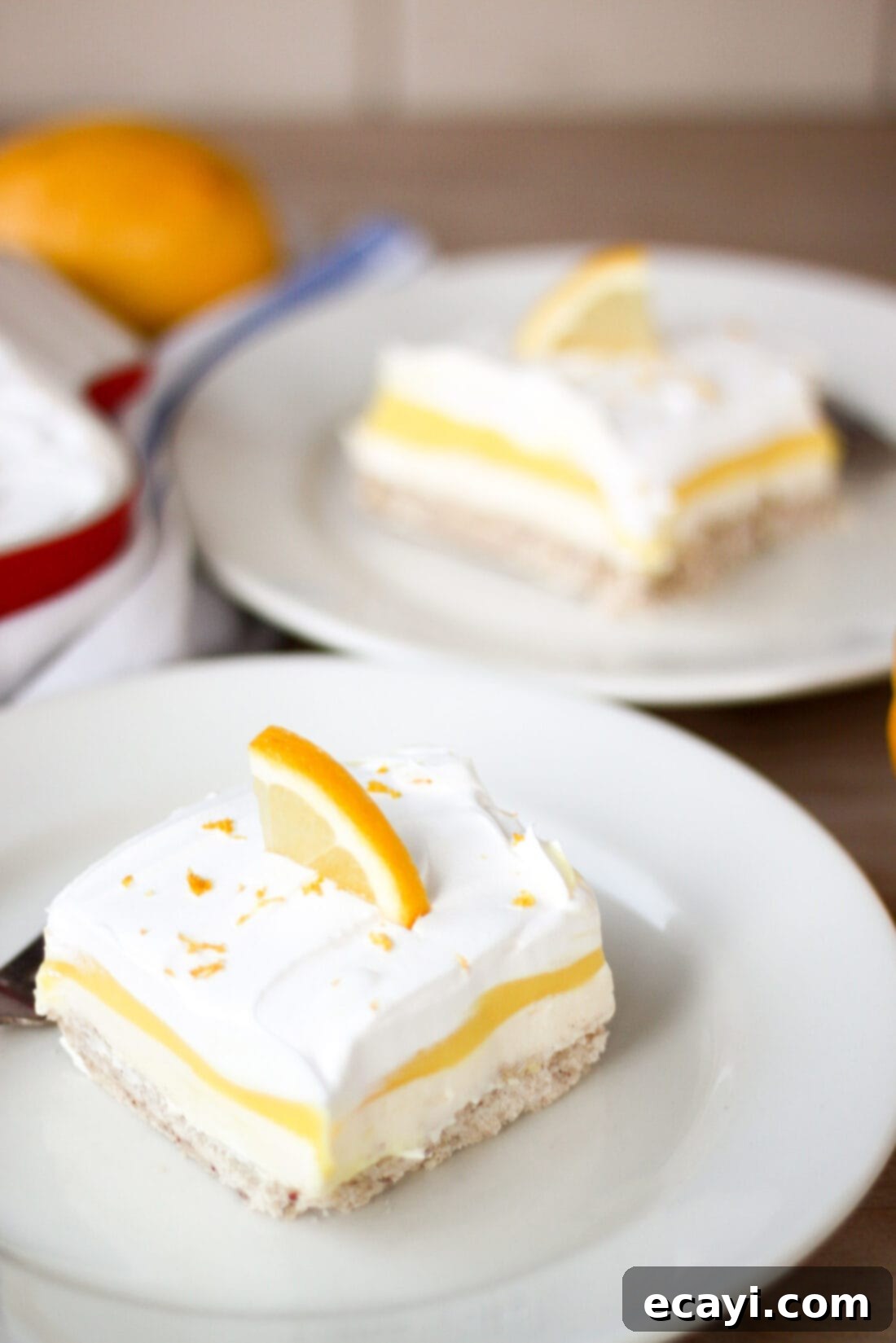 Lemon Lush. It's light and refreshing with 4 layers consisting of bottom pecan crust, lemon cream cheese, lemon pudding and topped with a whipped layer garnished with lemon zest. #lemonlush #lemondessert #lemonlasagna #nobake #onepandesserts #potluckdesserts #creamcheesedesserts #puddingdesserts  Two pieces of Lemon Lush on plates