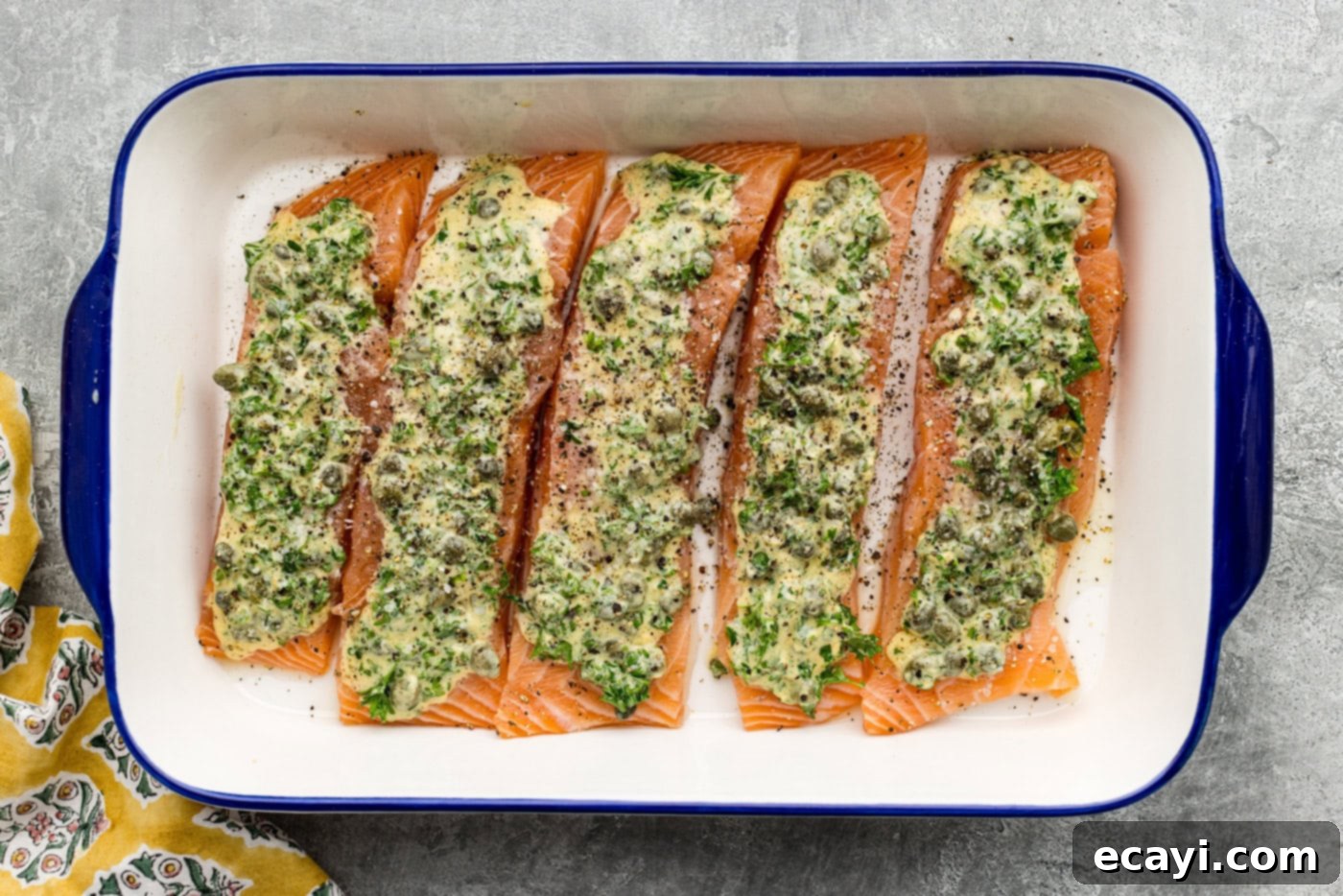 Zesty Lemon Caper Salmon 6 salmon filets in a baking dish topped with marinade and salt and pepper